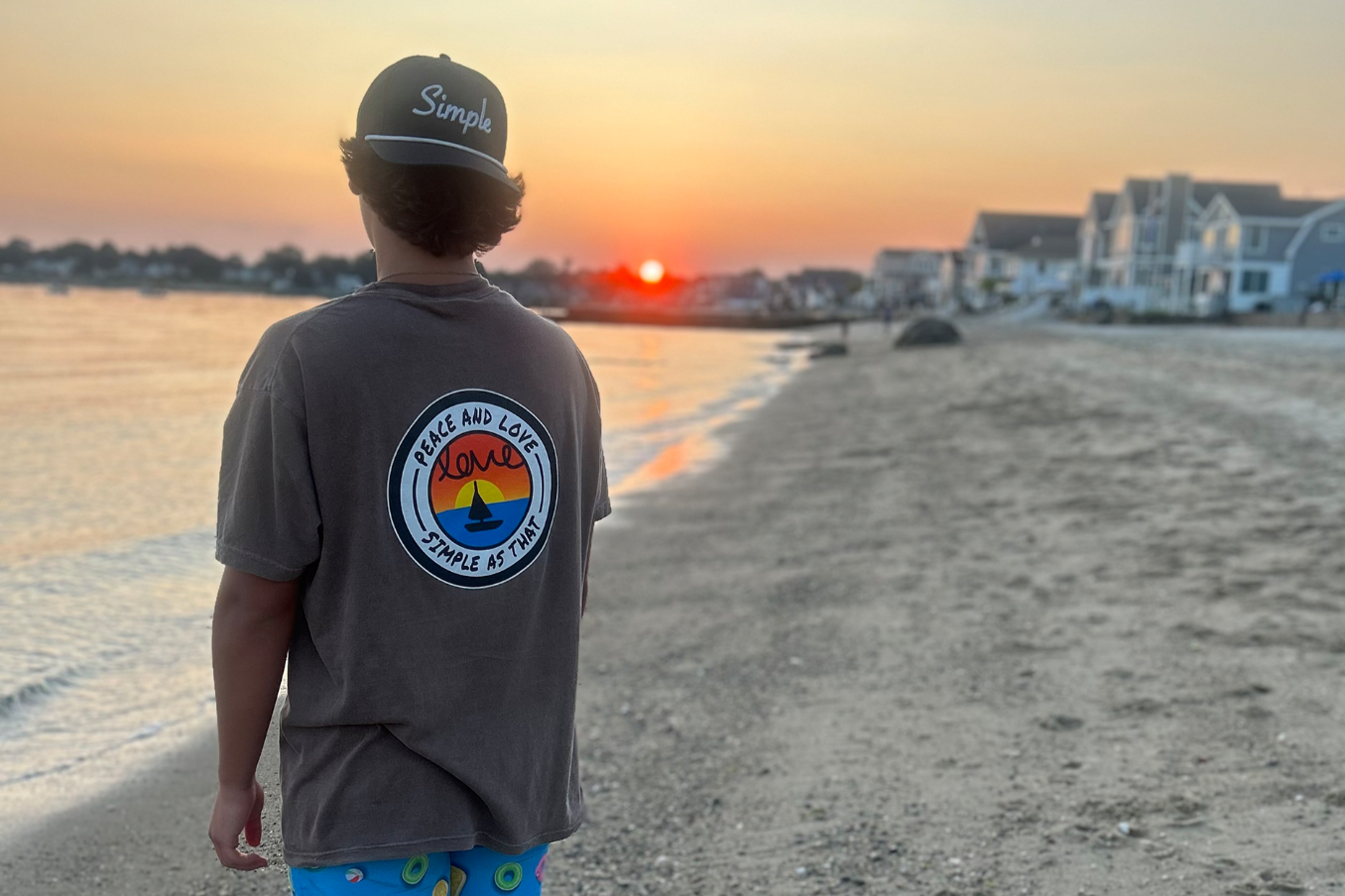 Simple As That – Model wearing the Peace and Love T-Shirt paired with a Simple Hat, standing on the beach at sunset. A relaxed, minimalist style that embodies peace, love, and authenticity. Explore custom apparel and unique streetwear designed for effortless fashion.