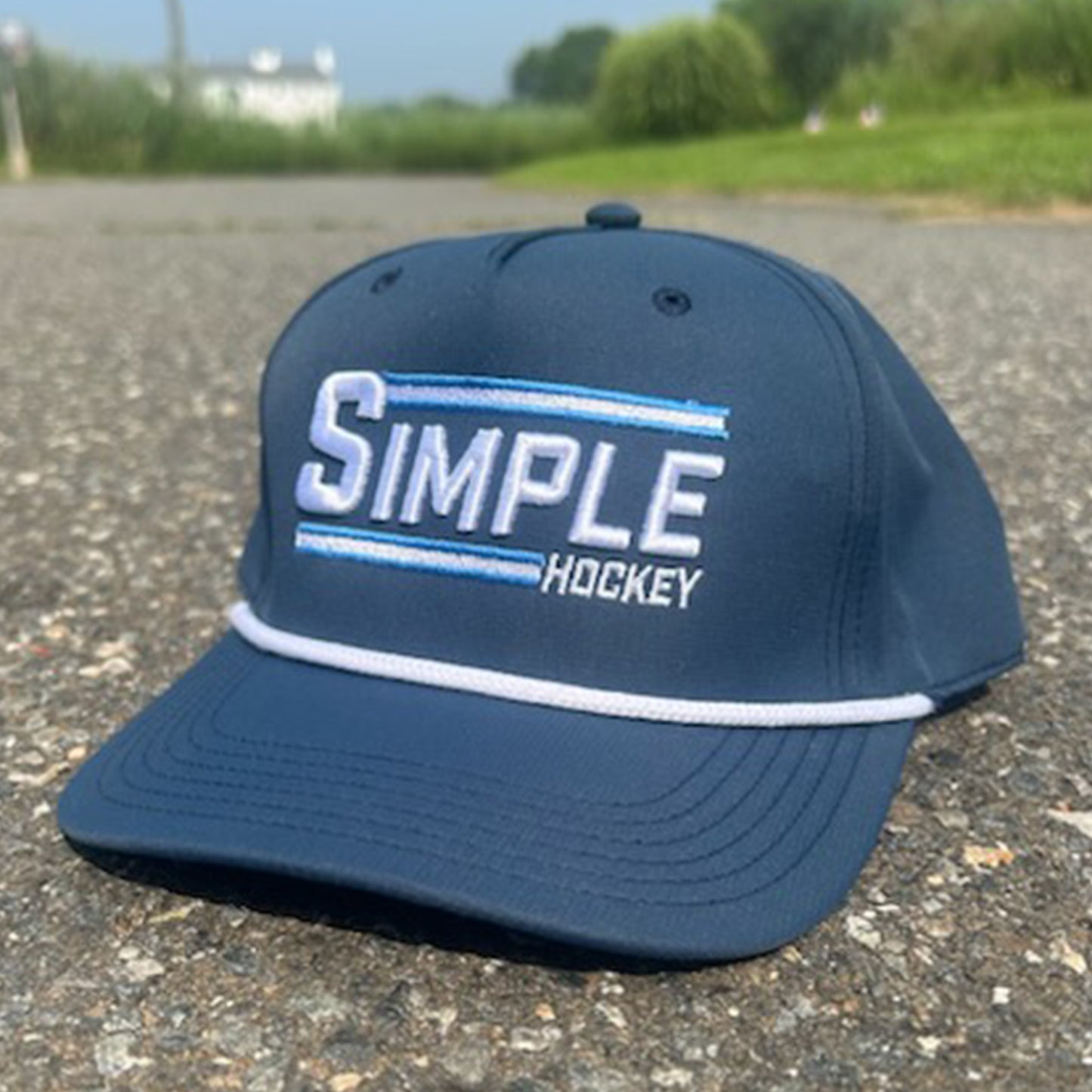 Navy blue 'Simple Hockey' rope hat featuring bold white and light blue embroidered 'SIMPLE' text with 'HOCKEY' below, highlighted by two horizontal stripes and a classic white rope detail across the brim. Snap back. It's really as Simple As That!