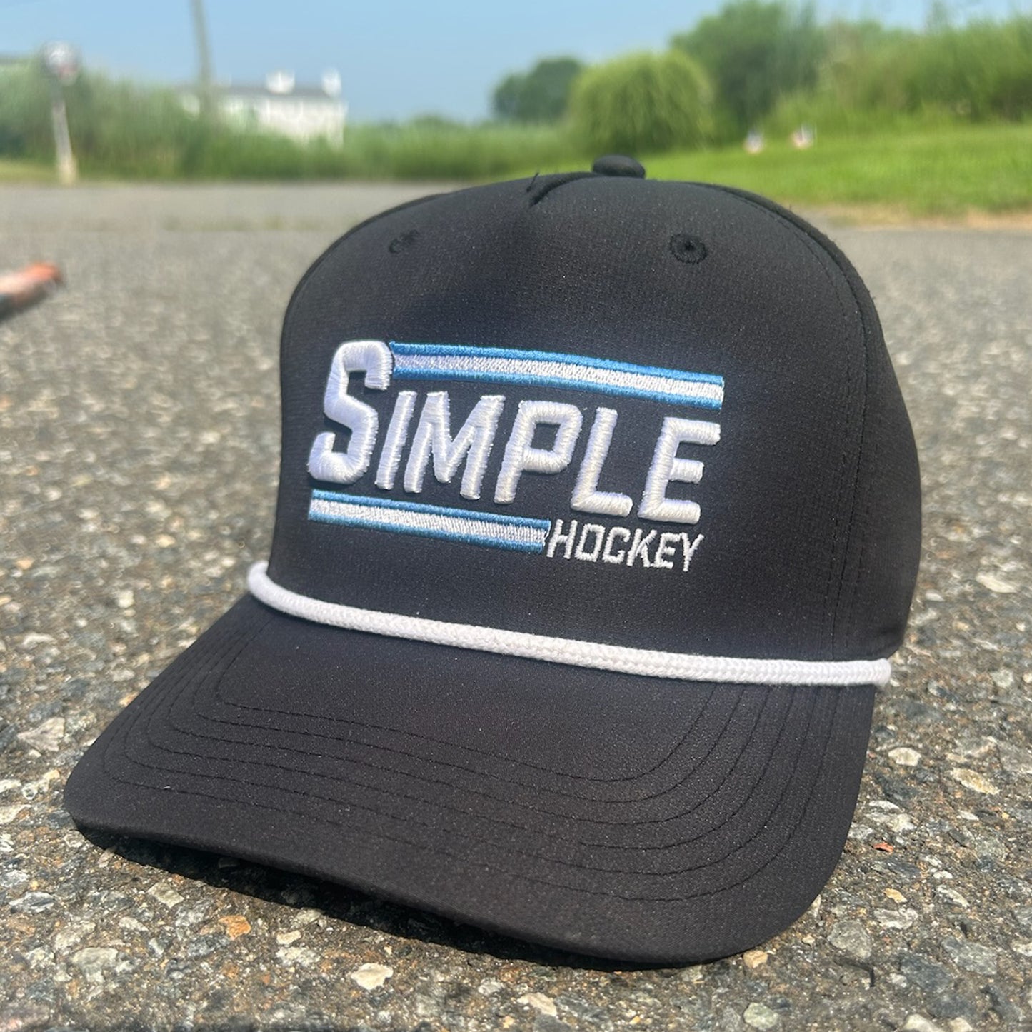 Black 'Simple Hockey' rope snap back hat featuring bold white and light blue embroidered 'SIMPLE' text with 'HOCKEY' below, highlighted by two horizontal stripes and a classic white rope detail across the brim. It's really as Simple As That!